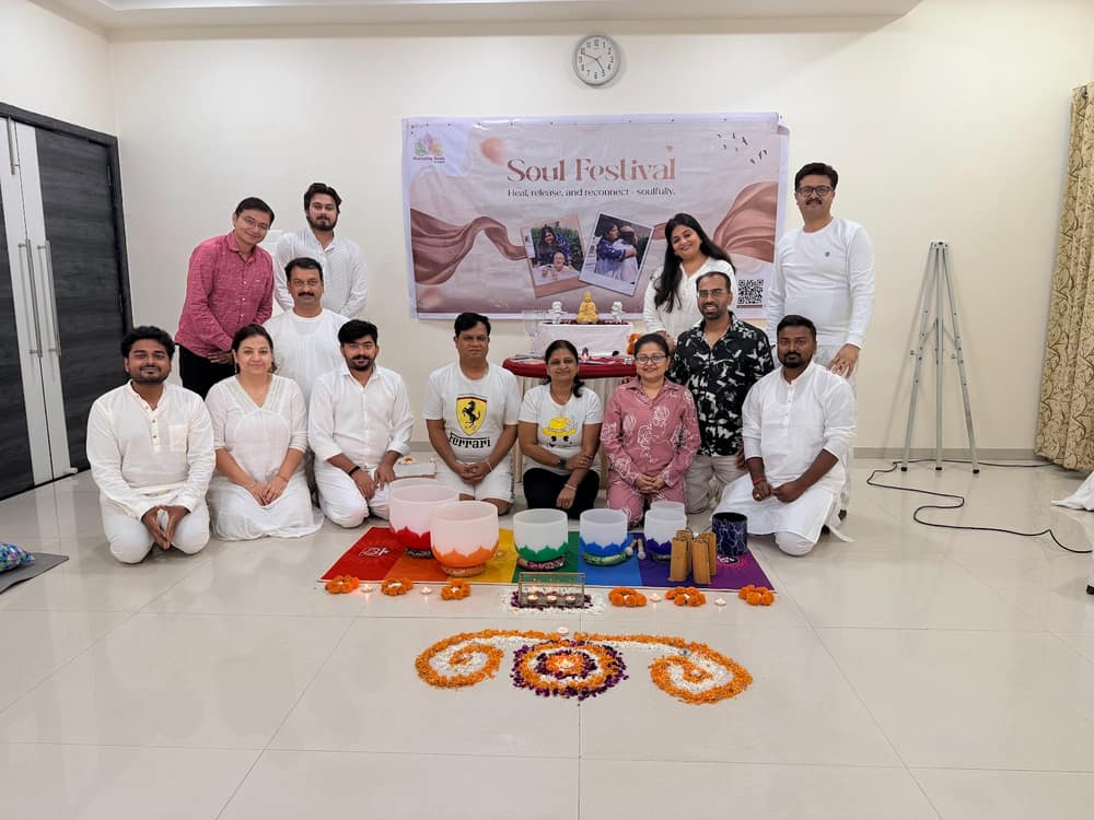 A Soul Festival group seated on the floor in white clothing behind a rangoli laid with singing bowls