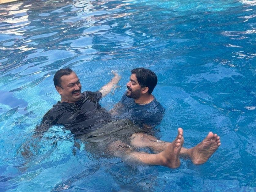 A facilitator supporting a participant floating on his back in a swimming pool during an aqua meditation session