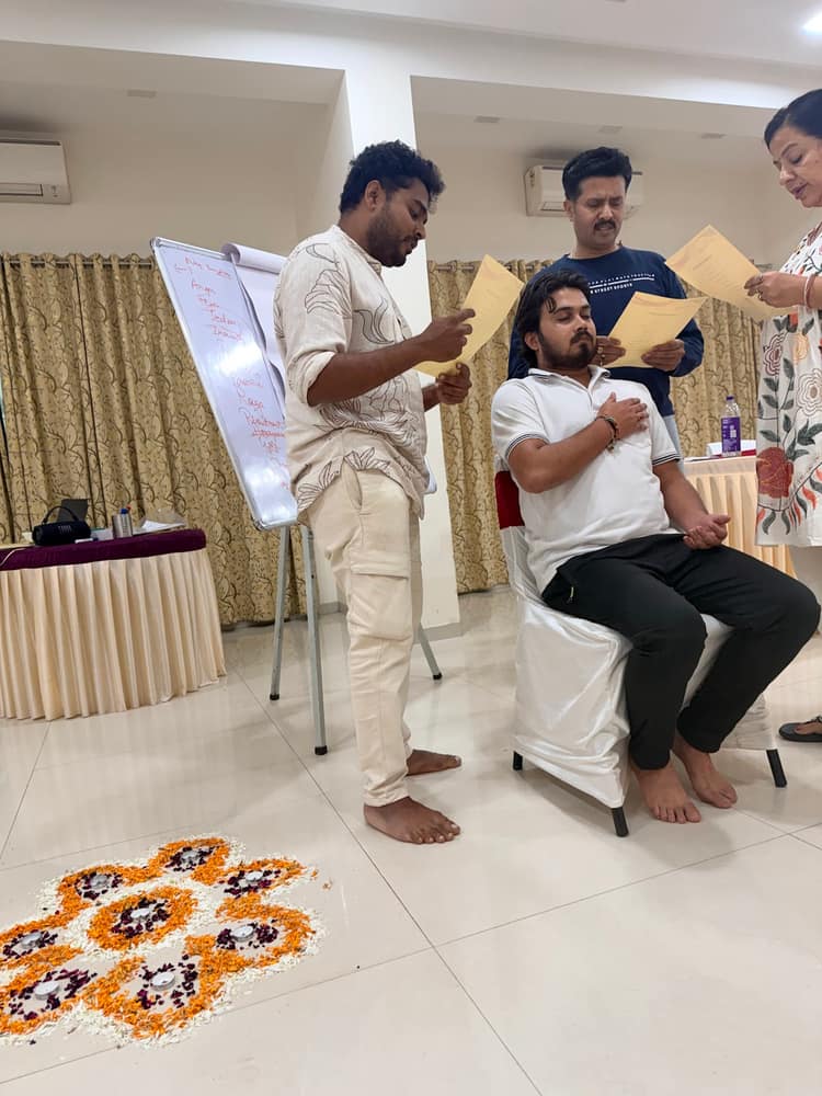 A participant presenting at a flip chart while another sits in the centre of the circle, marigold rangoli on the floor